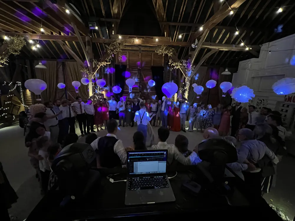 Guests circling the dance floor at a barn wedding, seen from behind the DJ booth
