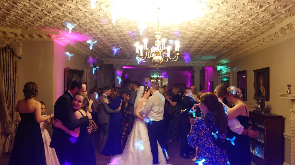 A first dance under an ornate ceiling, with guests around the floor and pink uplighting on the walls