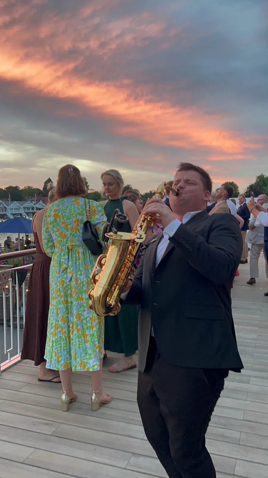 Saxophonist playing over the party at sunset on a waterside terrace