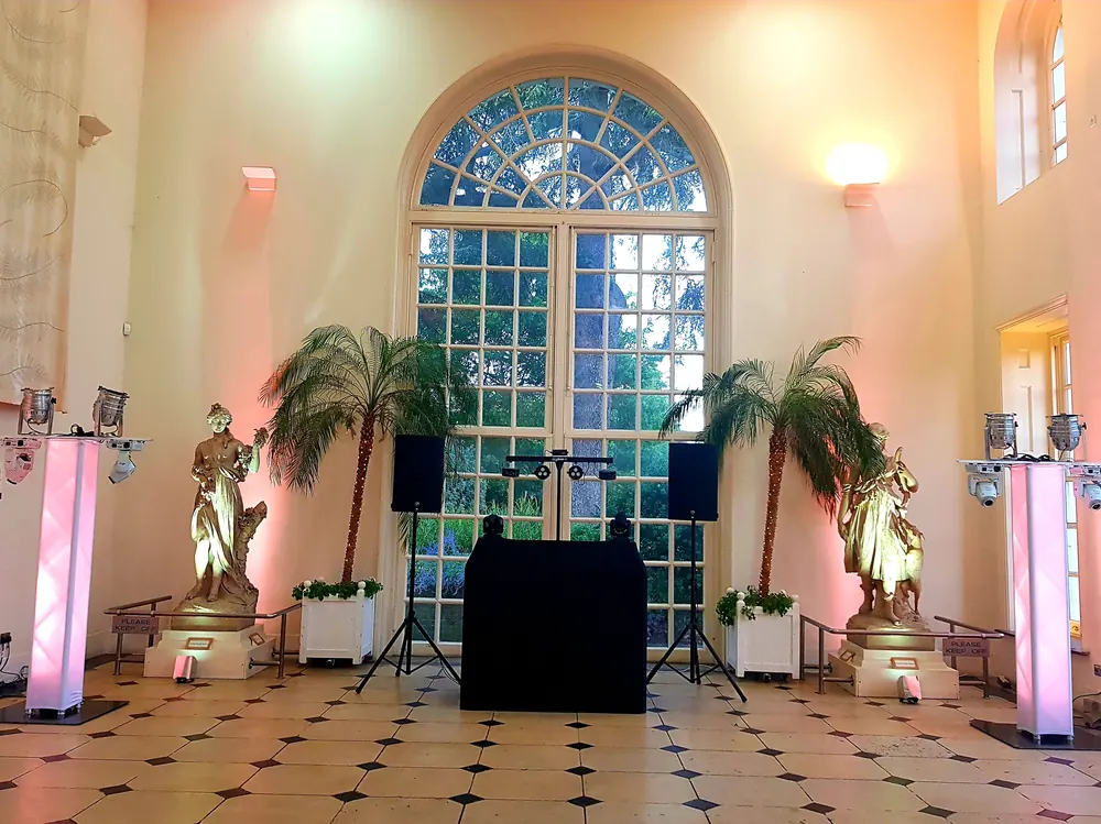 DJ booth set up beneath a tall arched window, with pink and white uplighting either side of the floor